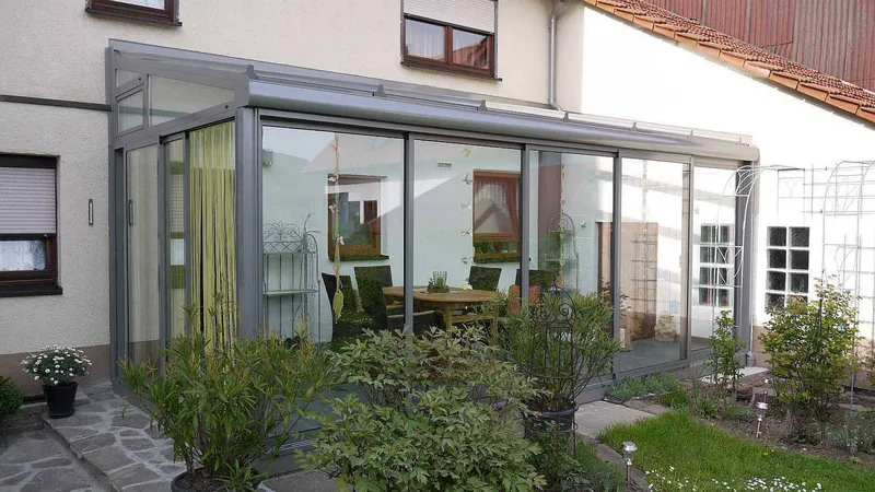 Ogród zimowy z szarych profili aluminiowych i szkła, w środku zestaw jadalniany