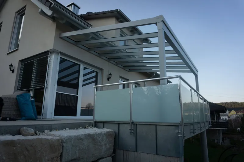 Zadaszenie podwyższonego tarasu ze szklanym dachem i balustradą z matowego szkła