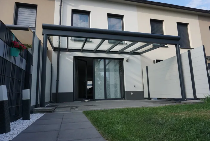 Antracytowe zadaszenie ze szklanym dachem i jasną ścianką osłonową przy domu szeregowym